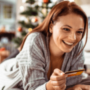 woman sitting behind Christmas tree and shopping online while holding a credit card in her hand
