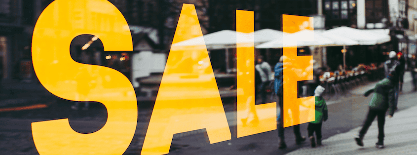 Großer Banner in einem Kaufhaus-Schaufenster, auf dem in gelben Großbuchstaben auf schwarzem Grund "SALE" steht.